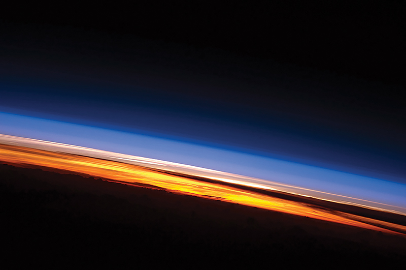Sunset on the Indian Ocean as seen by astronauts aboard the International Space Station. The image presents an edge-on, or limb view, of Earth’s atmosphere as seen from orbit. Earth’s curvature is visible along the horizon line, or limb, that extends across the image from center left to lower right. Above the darkened surface of Earth, a brilliant sequence of colors roughly denotes several layers of the atmosphere.