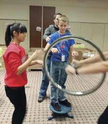Kathleen Miller-Chell and Tye Williams coach a young man in how to use the spinning wheel on the platform to experience angular momentum.